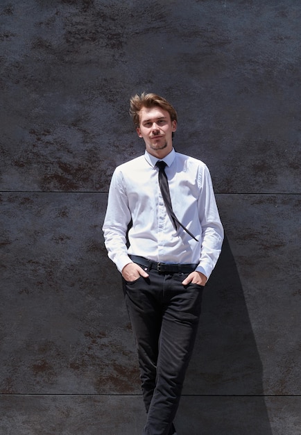 portrait of startup businessman in a white shirt with a black tie standing in front of gray wall outside