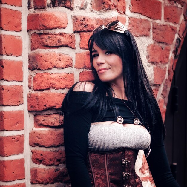 Photo portrait of steampunk woman standing against brick wall