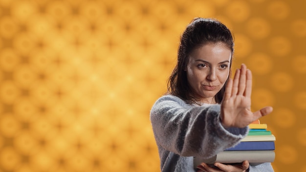 Photo portrait of stern woman holding stack of books doing stop sign gesturing