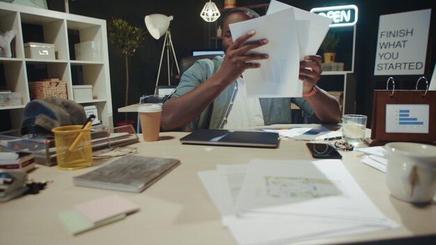 Portrait of stressed african american guy finding mistake in papers at hipster workplace Upset hipster guy falling into despair in office Exhausted male professional failing with documents indoors