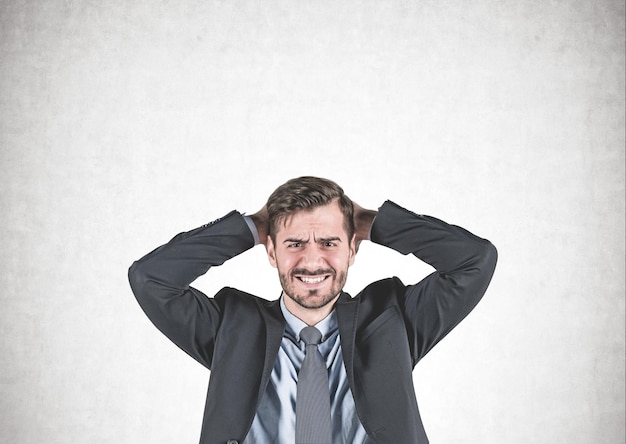 Photo portrait of stressed young businessman in suit standing with clenched teeth and painful expression near concrete wall