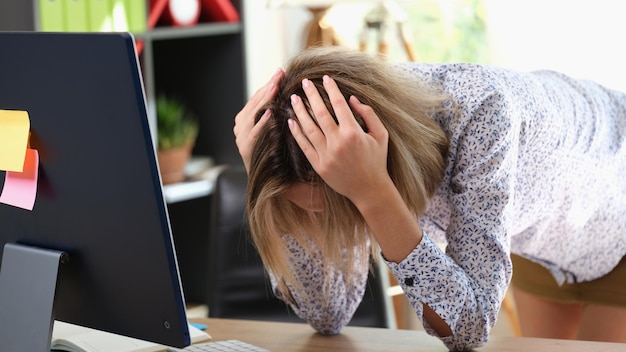 Ritratto di donna stressante chinarsi sul tavolo e tenendo la testa con le mani in ufficio sconvolto