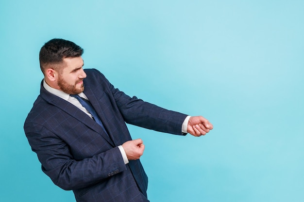 Portrait of strong ambitious businessman in suit pretending to pull invisible rope concept of hard working striving and efforts to achievements Indoor studio shot isolated on blue background