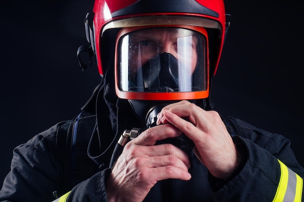 彼の手で斧チェーンソーを保持している耐火性の制服を着た肖像画の強い消防士黒の背景studio。頭の酸素マスクをクローズアップ