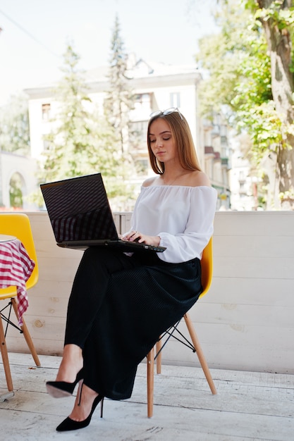 Portrait of a strong independent successful businesswoman wearing smart casual clothing and glasses working on a laptop in a cafe.