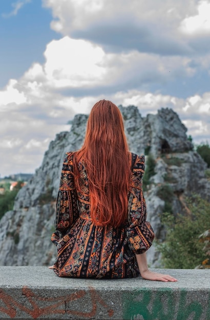 Photo portrait of a strongwilled free strong redhaired woman in an ethnic dress near a large stone a symbol of indomitability career fashion photo concept