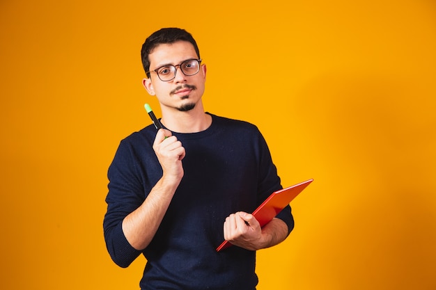 Portrait of student boy thinking and holding notebook on yellow background