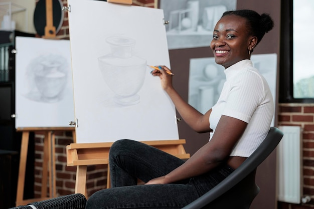 Portrait of student smiling and drawing sketch on canvas during creative art class. Young woman enjoying artwork lesson developing artistic new skills in creativity studio. New years resolutions