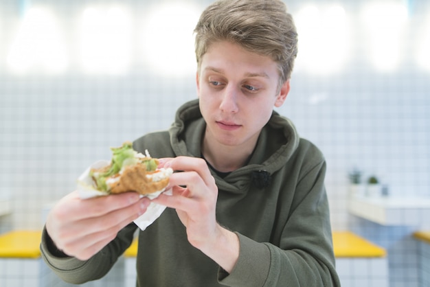 Photo portrait of a student who looks hungry at the sandwich in his hands.