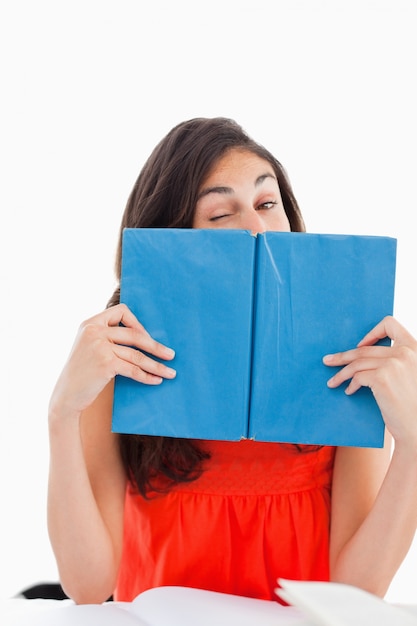 Portrait of a student winking behind a blue book