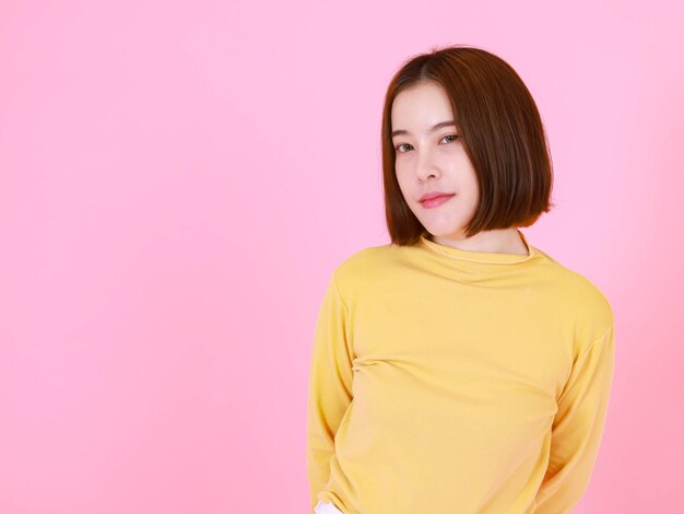 Portrait studio cutout shot of Asian young pretty short hair female model in yellow long sleeve shirt stand smile look at camera on pink background.