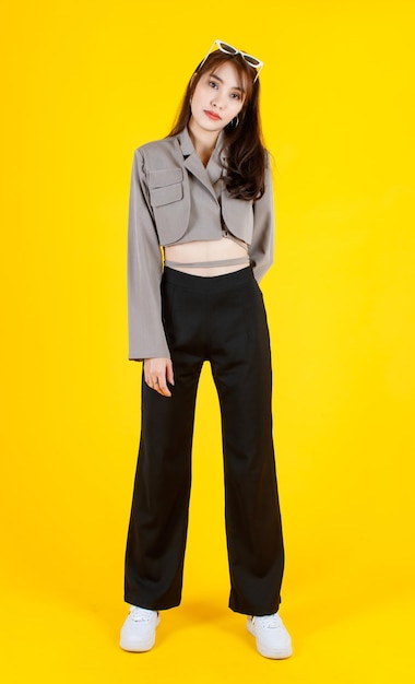 Портретная студия в полный рост азиатской городской модной современной модной длинноволосой женщины-хипстера-подростка модели на повседневной улице носит укороченную рубашку, стоящую и позирующую, глядя в камеру на желтом фоне.