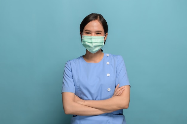 Foto foto dello studio del ritratto della maschera di protezione d'uso della giovane infermiera asiatica sull'azzurro.