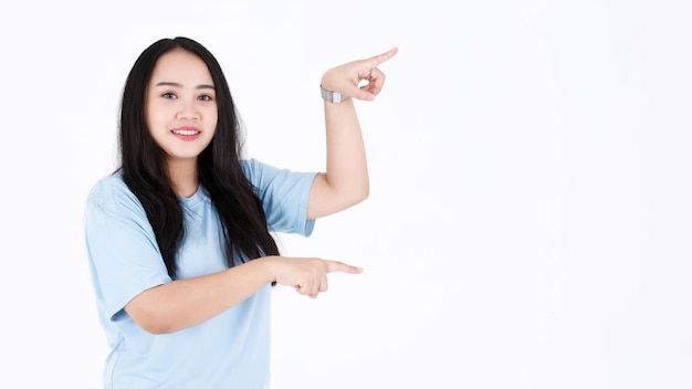 Colpo dello studio del ritratto di modello femminile asiatico giovane paffuto grassoccio lunghi capelli neri in maglietta casual blu e orologio da polso che tiene la mano che indica lo spazio vuoto che mostra la presentazione del prodotto su priorità bassa bianca.