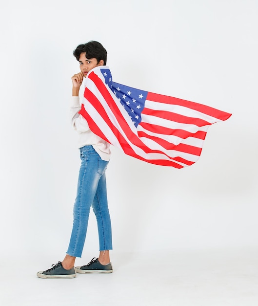 Portrait studio shot of Asian young LGBT gay bisexual homosexual male fashionable model in casual outfit and fashion sunglasses standing holding waving flying USA national flag on white background