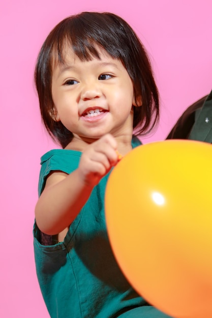 Portrait studio shot little cute Asian kindergarten preschooler girl daughter model in casual long dress holding colorful balloons on pink background