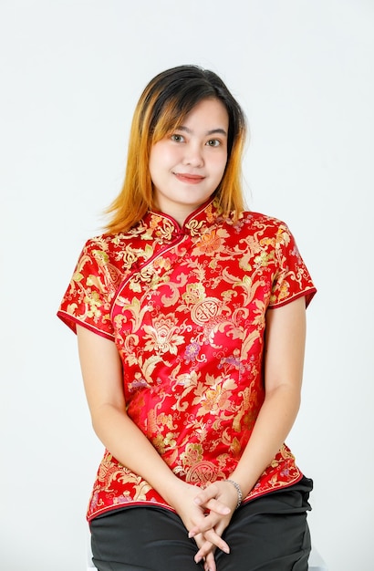 Portrait studio shot of millennial Asian young teen dyed hair female model wearing beautiful gold and red Chinese traditional cheongsam qipao shirt standing smiling look at camera on white background.