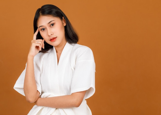 Portrait studio shot of millennial young Asian short black hair female model in white shower rope standing smiling look at camera posing pose in advertising action on brown background.