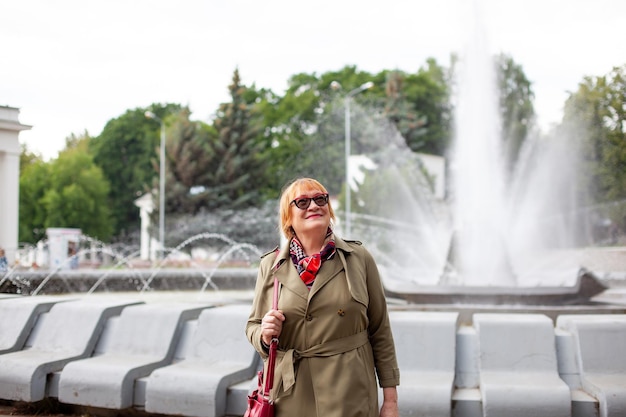 Portrait of stylish 65yearold woman on background of fountain in park