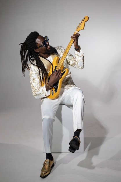 портрет стильного африканца в белом костюме и солнцезащитных очках с электрической гитарой