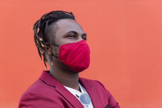 Portrait of a stylish african man with protective mask to match his suit on a red background