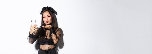 ゴシックメイクとハロウィーンの衣装を着たスタイリッシュなアジアの女性ブロガーのポートレートは、エアキスを送信します