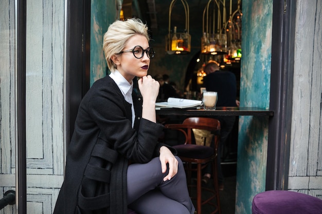 Portrait of stylish beautiful blonde woman thinking and sitting in cafe alone