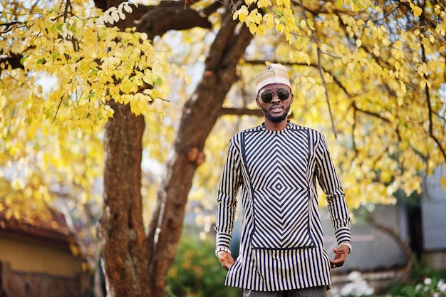 Portrait of stylish black african american man at hat and sunglasses against sunny autumn fall background Rich people in africa at traditional dress