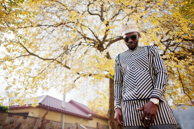 Portrait of stylish black african american man at hat and sunglasses against sunny autumn fall background Rich people in africa at traditional dress