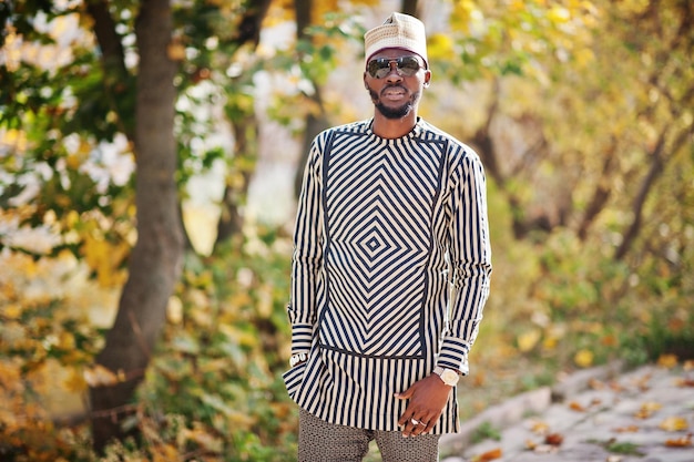 Ritratto di elegante uomo afroamericano nero con cappello e occhiali da sole su sfondo autunnale soleggiato