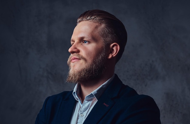 Portrait of stylish blond bearded male dressed in a suit over grey background.