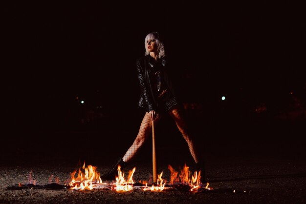 Ritratto di giovane donna bionda elegante grunge con il club vicino al fuoco