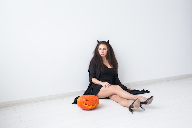 Portrait of a stylish brunette woman with halloween pumpkin over light background with copy space