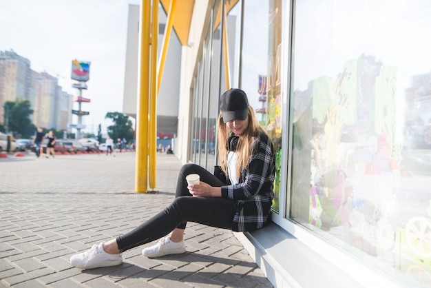 Ritratto di un elegante abbigliamento casual seduto alla vetrina con una tazza di caffè in mano e guardando verso il basso.