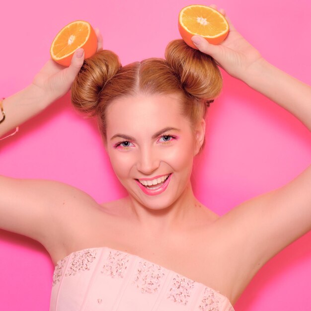 Portrait of stylish cute young blonde woman with oranges on pink background