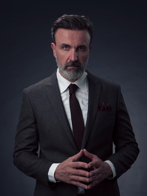 Portrait of a stylish elegant senior businessman with a beard and casual business clothes in photo studio isolated on dark background gesturing with hands. High quality photo