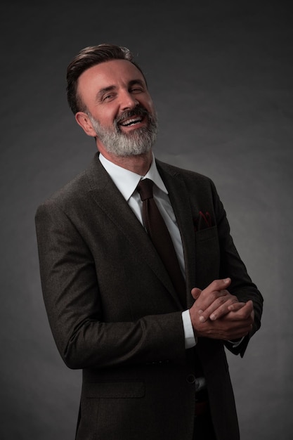 Портрет стильного элегантного старшего бизнесмена с бородой и повседневной деловой одеждой в фотостудии, изолированной на темном фоне, жестикулирующей руками. Фото высокого качества