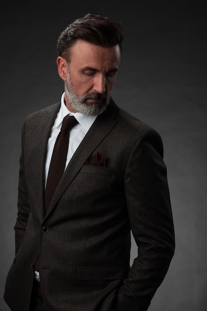 Portrait of a stylish elegant senior businessman with a beard and casual business clothes in photo studio isolated on dark background gesturing with hands. High quality photo