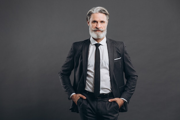 Portrait of a stylish and fashionable mature man in a gray suit. Business and trendy close-up concept on the grey wall.