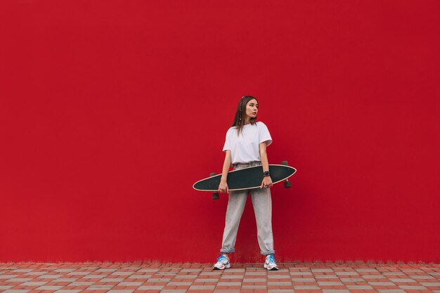 portrait of a stylish female skater holding her skateboard and standing on a city street