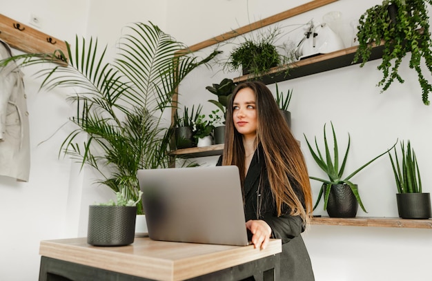 Portrait of a stylish girl in a suit sits at a table in a stylish cozy cafe and works on a laptop