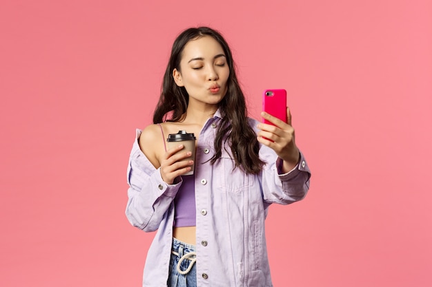Photo portrait of stylish good-looking female blogger, lifestyle internet influencer taking selfie with take-away coffee from her favorite cafe, hold mobile phone, pouting for kiss and close eyes