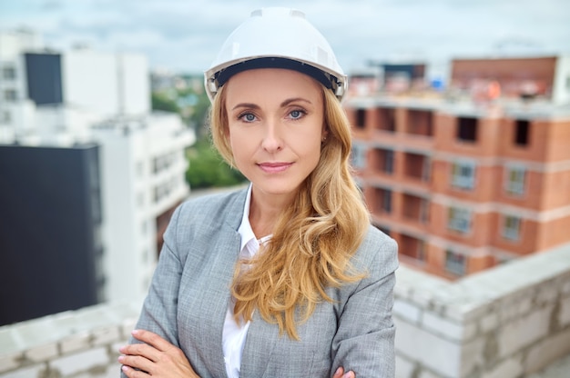 Portrait of a stylish lovely blonde tranquil confident female supervisor wearing a hardhat on the construction site