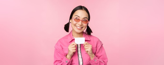 Портрет стильной современной азиатской девушки показывает кредитную карту со скидкой и выглядит довольным, платя бесконтактно