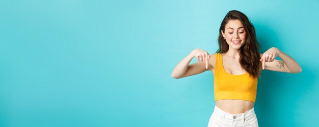 Portrait of stylish natural girl in summer crop top pointing and looking down with dreamy smile seei