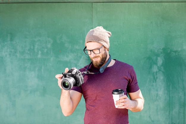 Photo portrait of a stylish photographer dressed casual in t-shirt and hat standing with camera on the green background