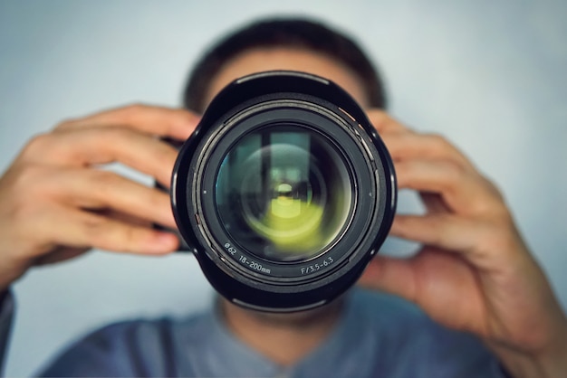 Photo portrait of a stylish photographer and hat standing with camera on the blue background. young photographer paparazzi looking at the camera. the moment of photographing. camera close up