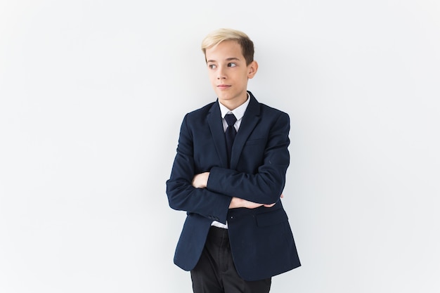 Portrait of stylish school boy teenager in white shirt and jacket against white surface with copy