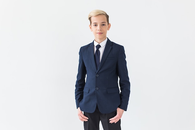 Portrait of stylish school boy teenager in white shirt and jacket against white wall with copy space