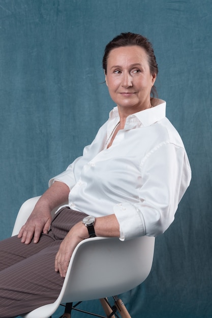 Portrait of a stylish senior woman officially dressed sitting on a chair and smiling.